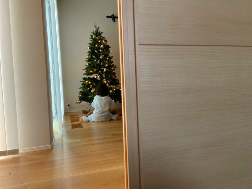 娘がクリスマスツリーの前でプレゼントを開けている画像